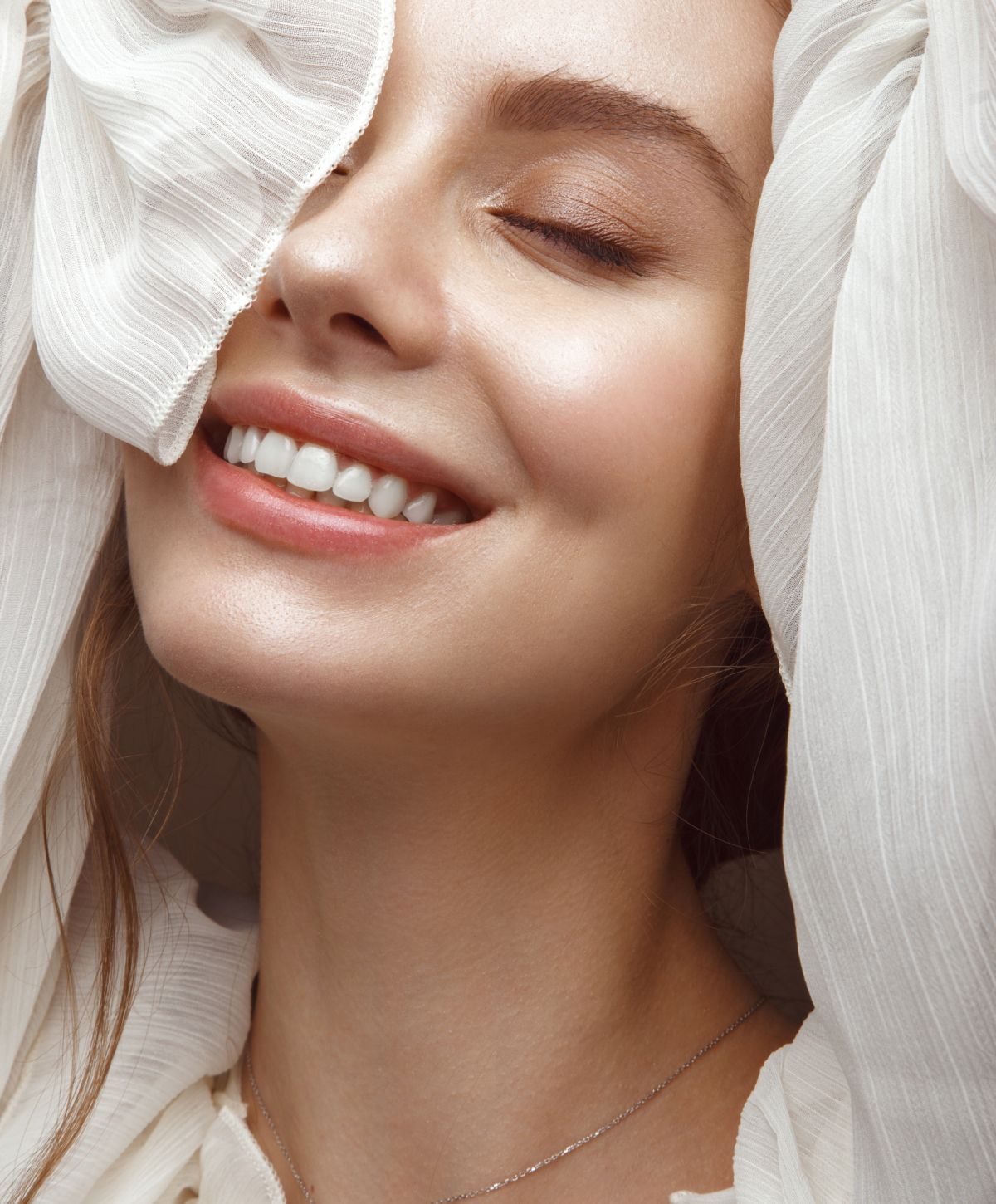 Smiling woman in white fabric, soft lighting.